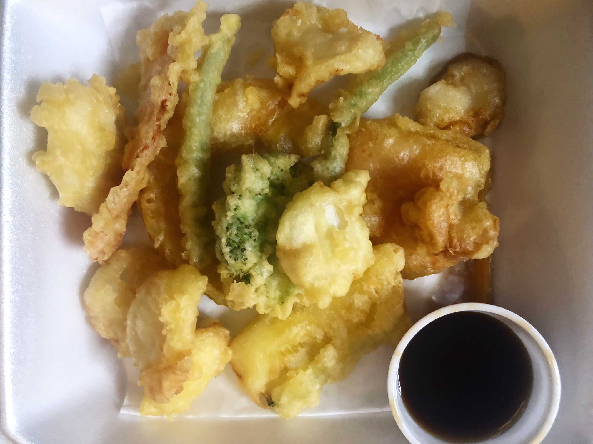 In a white styrofoam container, there are tempura scallops and tempura veggies plus a small cup of dipping sauce. Photo by Alyssa Buckley.