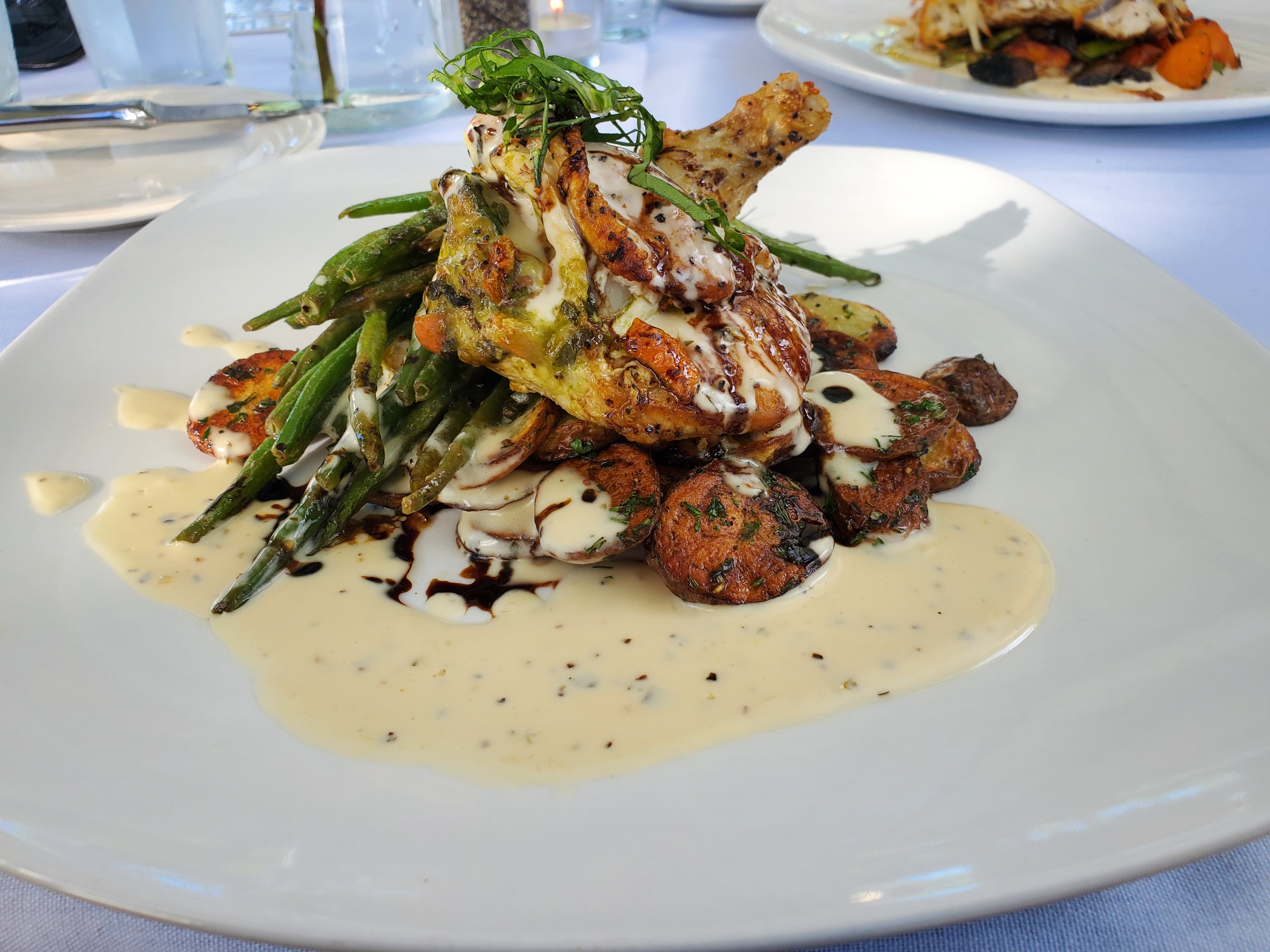 A beautifully plated dish of Caprese stuffed chicken with fingerling potatoes and haricots verts with a pale yellow citrus cream sauce pooling at the bottom. Photo by Carl Busch.