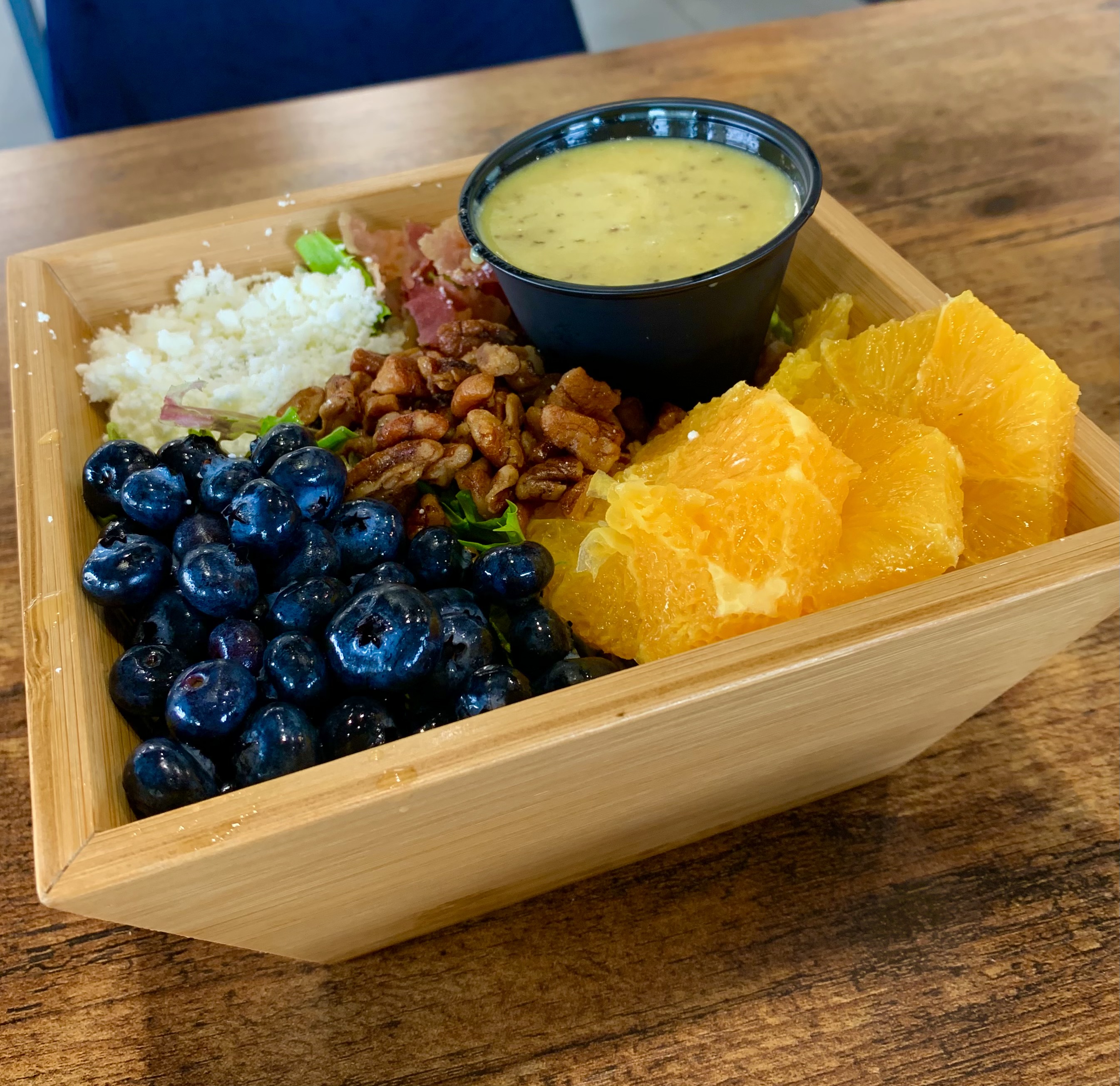 In a wooden square basket, there is a salad topped with lots of fresh fruit like blueberries and orange slices. Photo by Stephanie Wheatley.