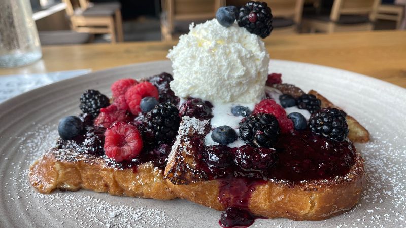 On a plate there are three slices of French toast with raspberries, blueberries, and blackberries on top with a mound of whipped cream melting into the toast. Photo by Alyssa Buckley.
