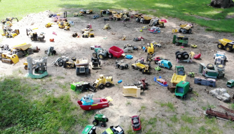 dozens of toy diggers and dozers sit in a huge sandbox 