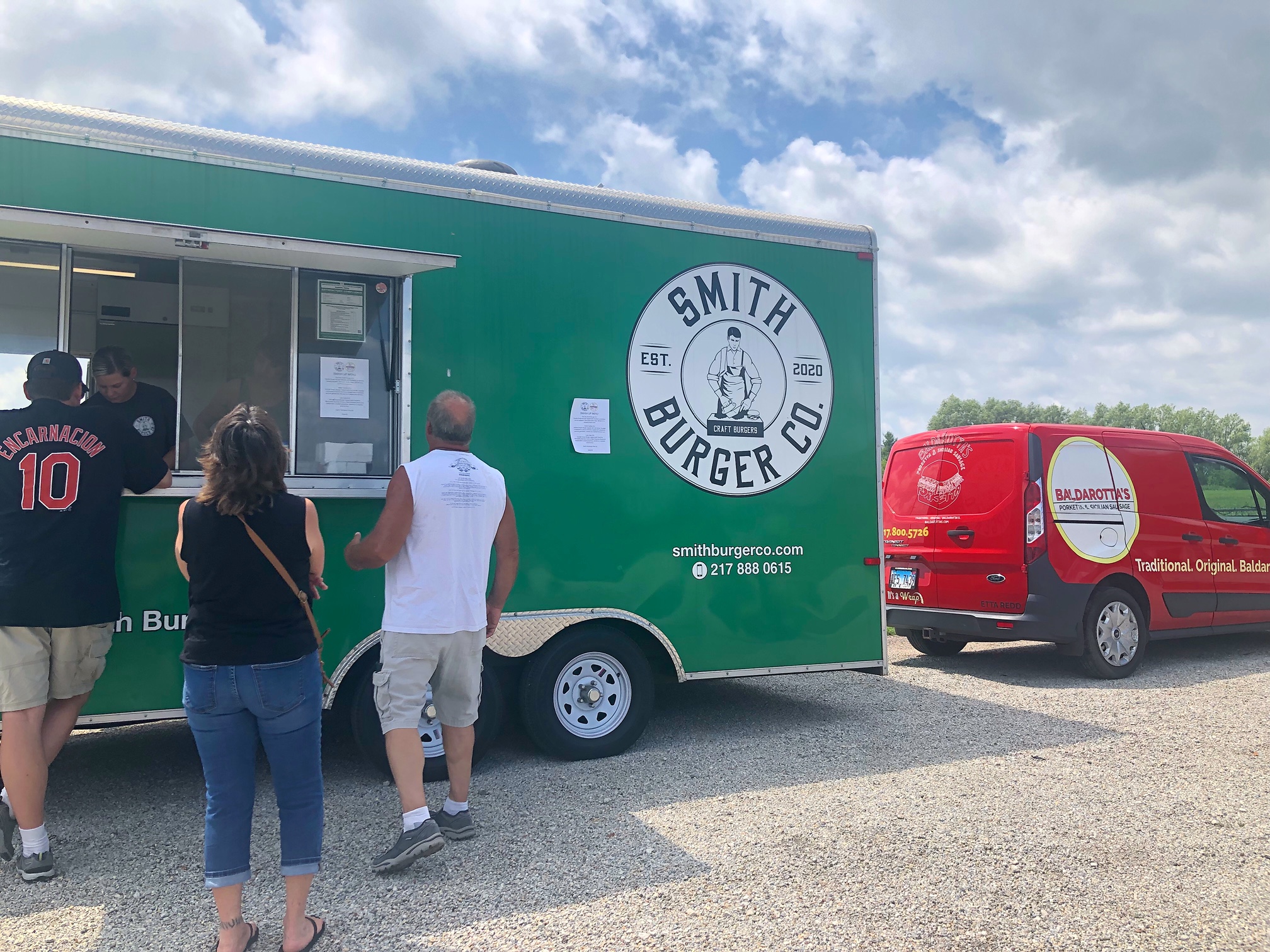 The green food truck of Smash Burgers sits parked beside the red van of Baldarotta's in the gravel lot by Riggs. Photo by Alyssa Buckley.