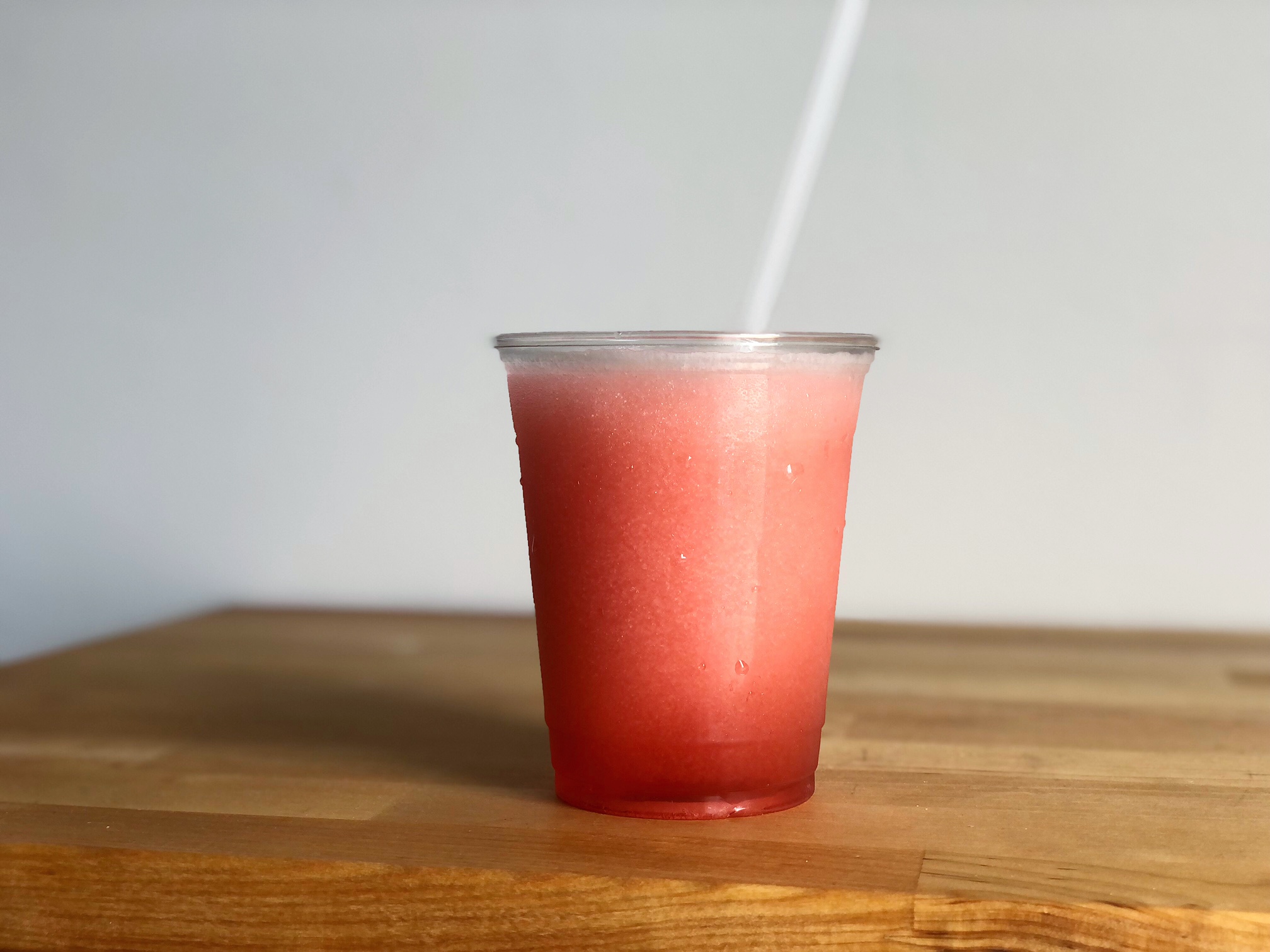 On a butcher block counter, there is a pink Aperol spritz slush from Art Mart in a plastic to go cup with a plastic straw. Photo by Alyssa Buckley.