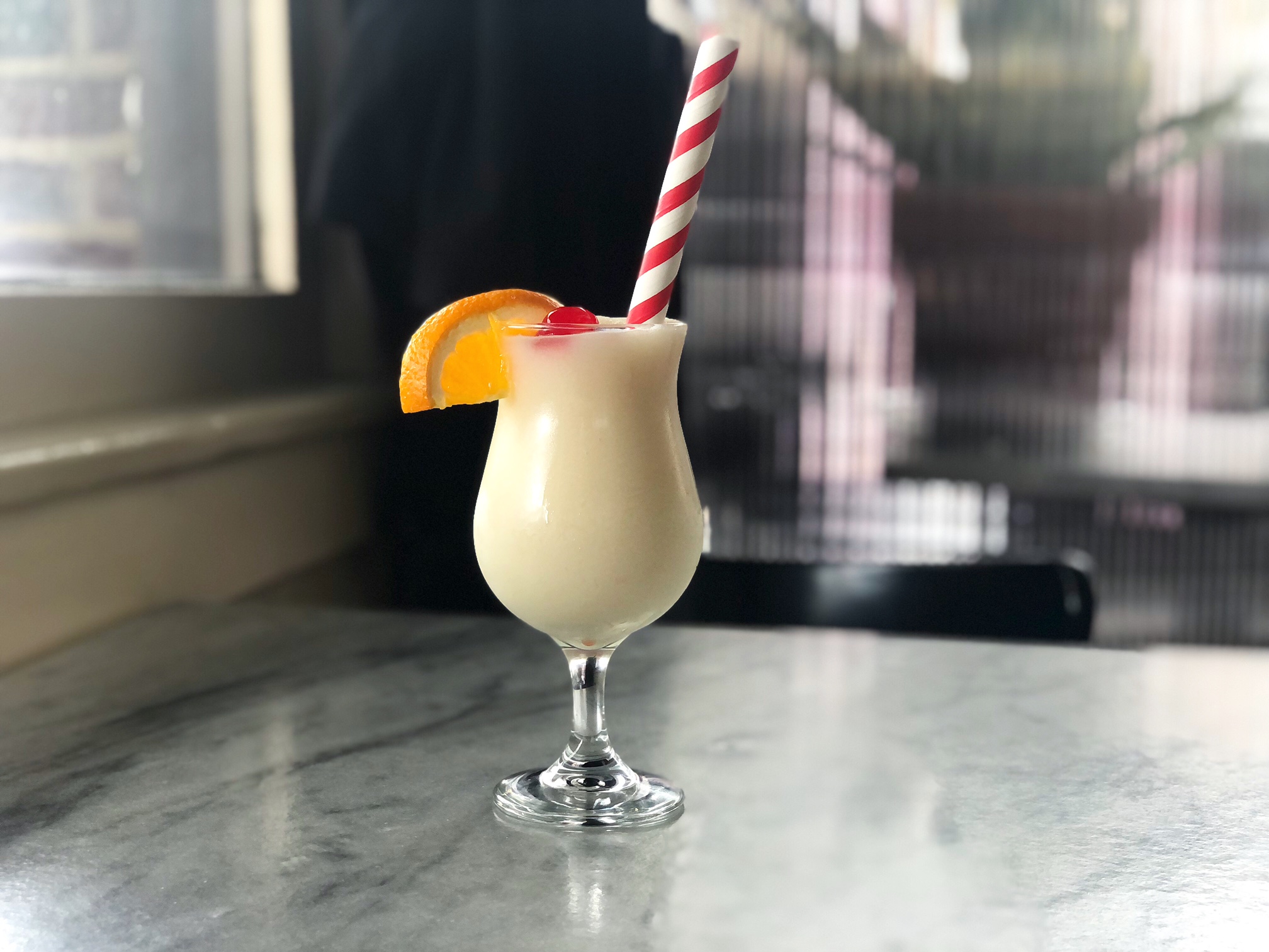 On a white marbled table at Farren's in Downtown Champaign, there is a white frozen colada slush with a striped straw. Photo by Alyssa Buckley.