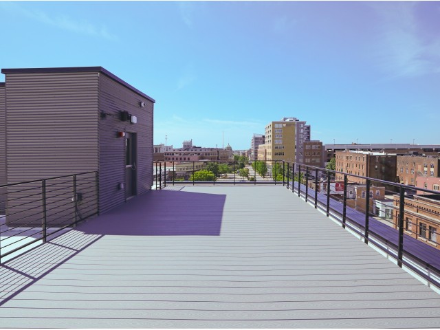 A rooftop of a building. The roof is flat and gray, and surrounded by black fencing. There is a small brown extension of the building with a door leading inside. Photo from 520 Neil website.