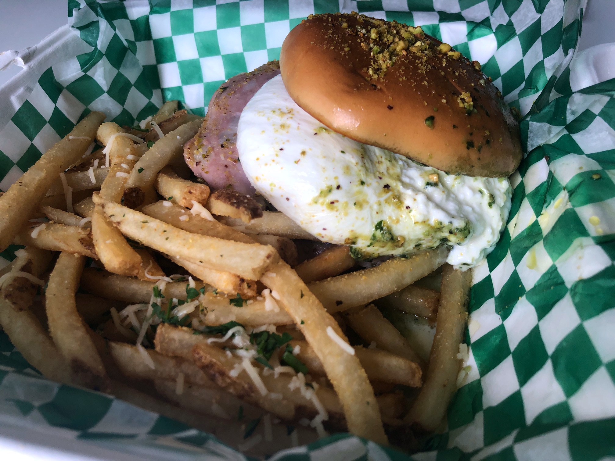 In a basket lined with white and green checkered paper, there is a burrato burger beside a large portion of long french fries. Photo by Alyssa Buckley.