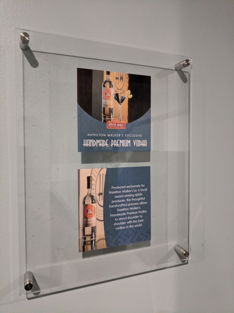 A flyer with a bottle of vodka and text is behind clear plastic, hanging on a gray door. Photo by Tom Ackerman.