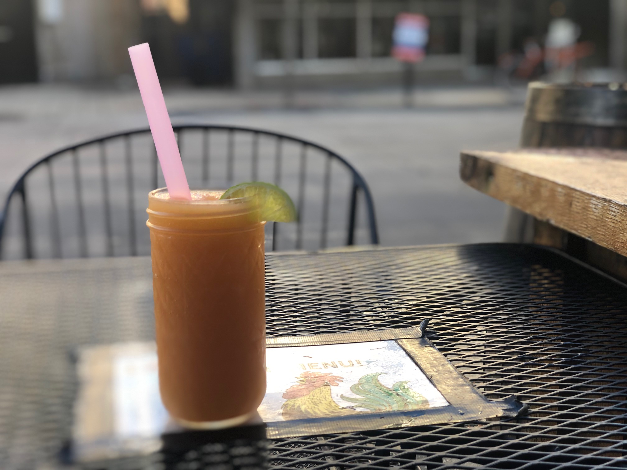 On a black outdoor table with a tape white piece of paper with a rooster, there is a mason jar filled with Watson's orange Protect Ya Nectar slush. Photo by Alyssa Buckley.