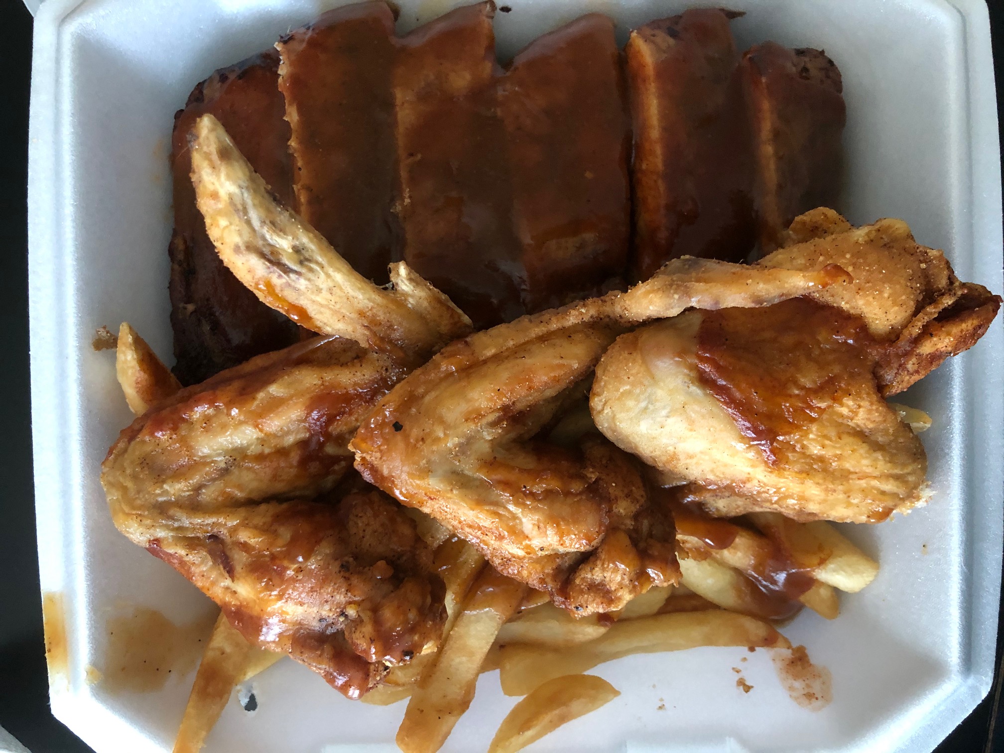 In a styrofoam container, there are three large wings over fries and a slab of ribs from Wood N Hog. Photo by Alyssa Buckley.