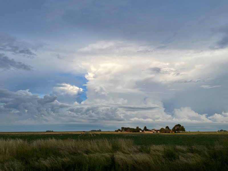 A cloudy early evening sky sits above an expanse of prairie and farm field. Photo by Andrew Pritchard.