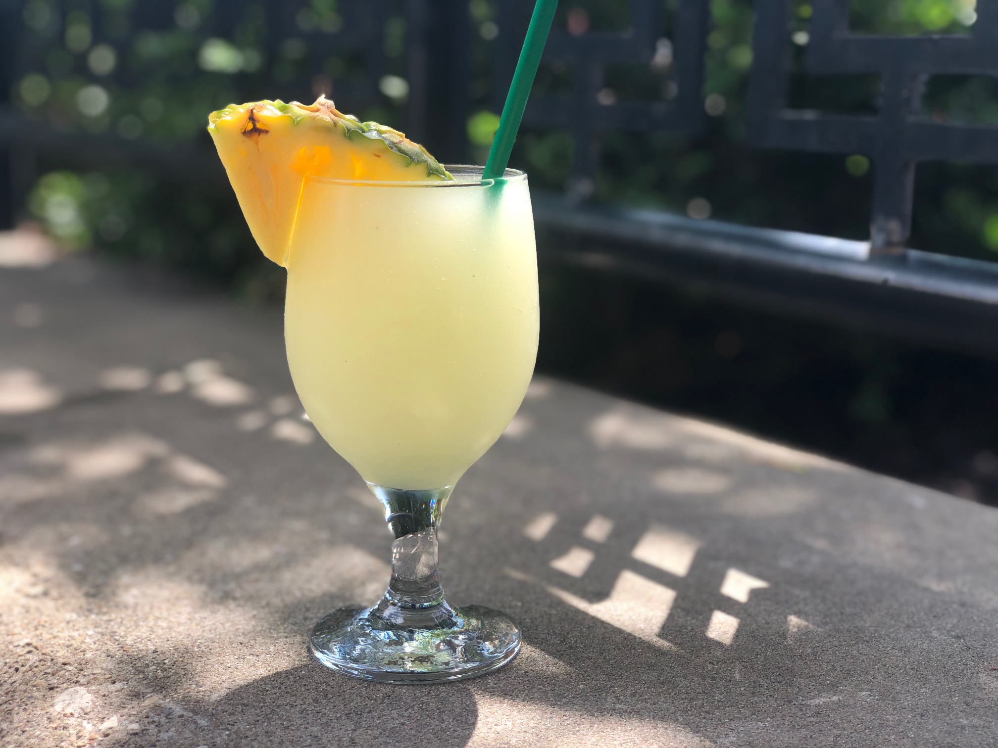 On a concrete ledge at Esquire's patio in Downtown Champaign, there is a wine glass filled with a yellow frozen pineapple margarita with a slice of pineapple as a garnish on the left side. Photo by Alyssa Buckley.