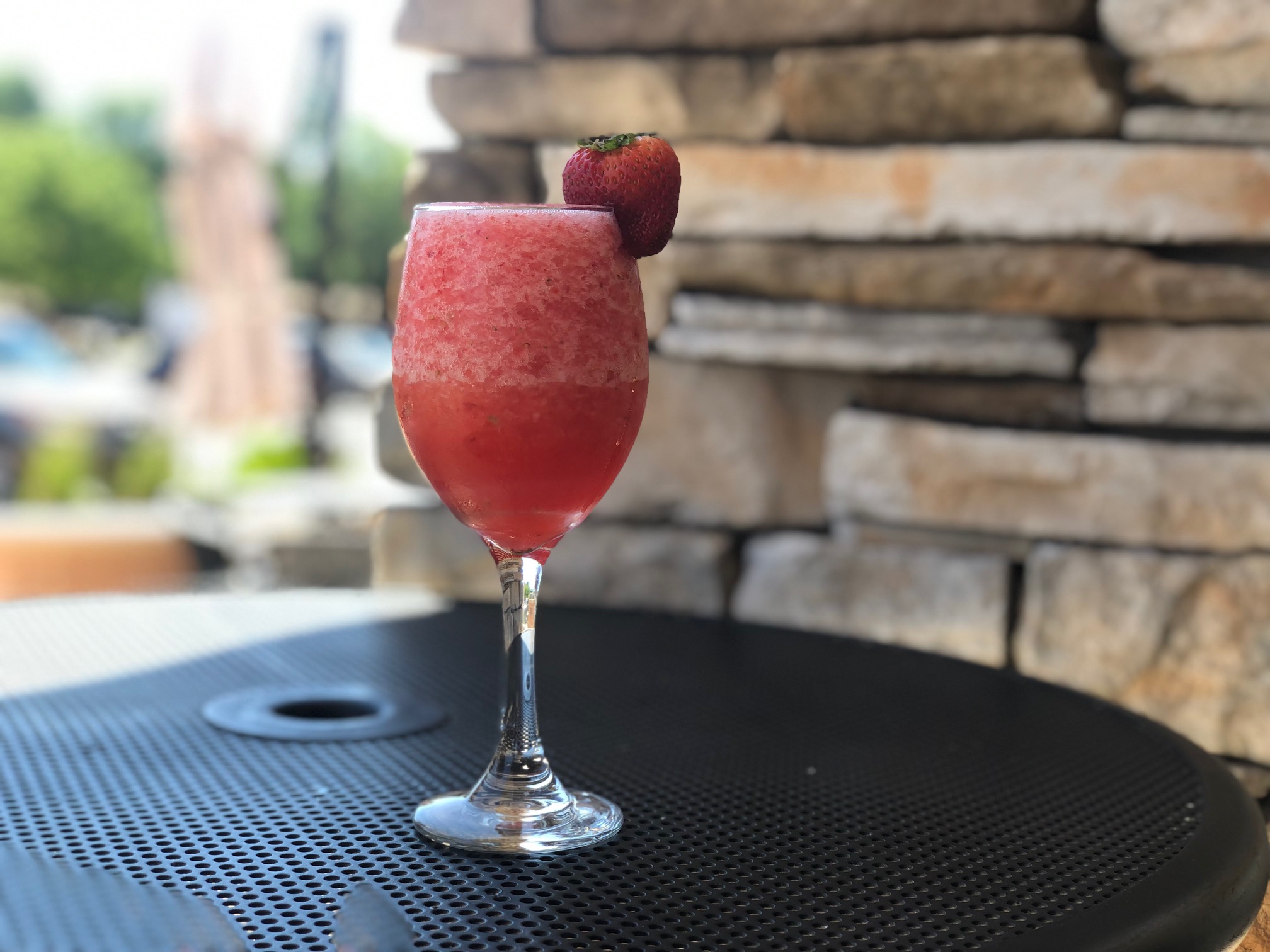 On a black patio table at Baxter's American Grill in Champaign, there is a wine glass filled with a strawberry iced drink with a full strawberry as a garnish on the right side. Photo by Alyssa Buckley.