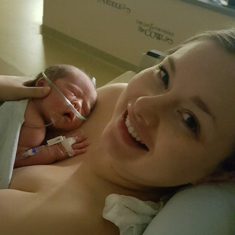 A woman with blonde hair is laying in a hospital bed and holding a newborn baby against her chest. The baby has a tube in his nose. Photo provided by Paige Raab.