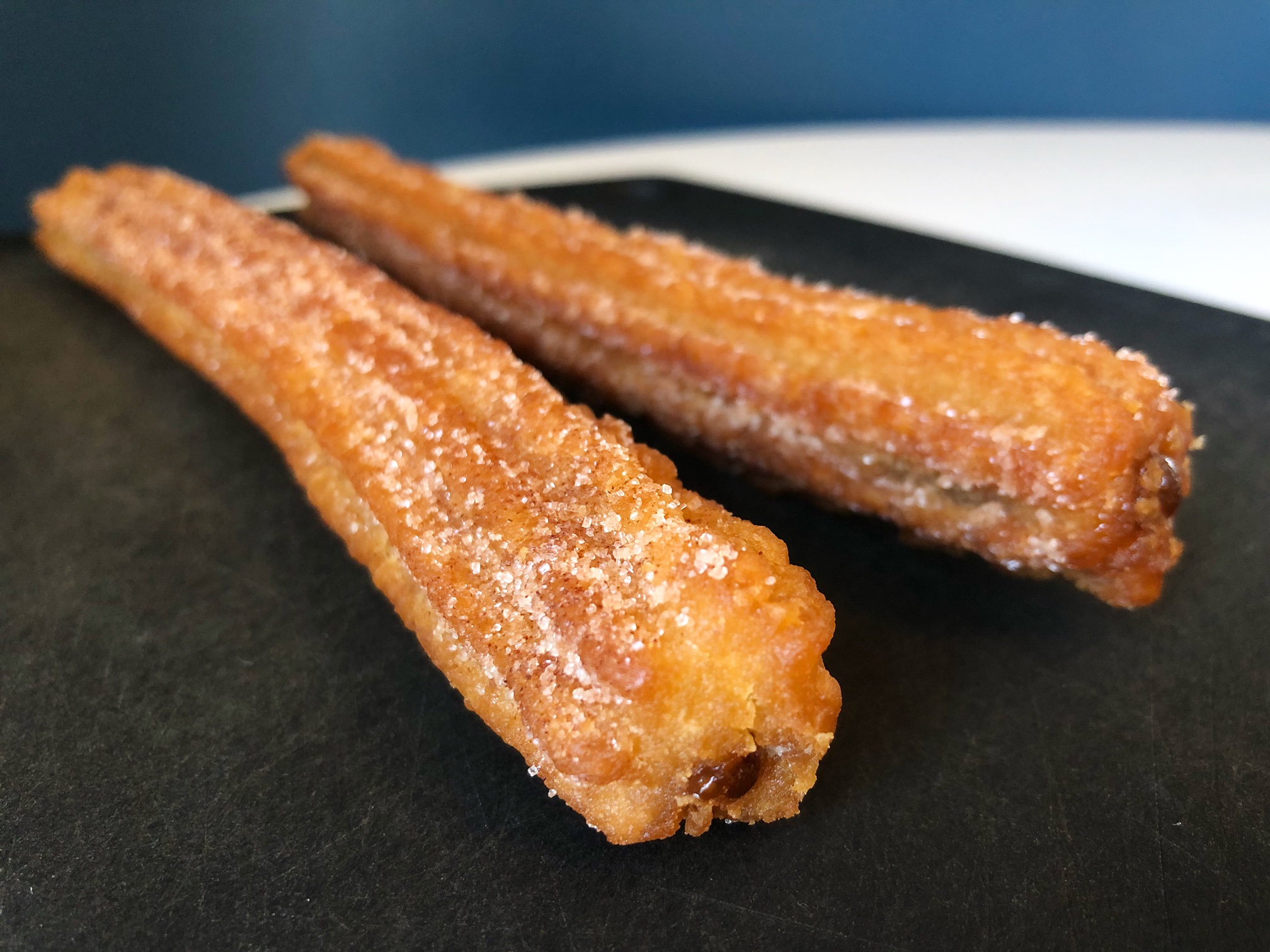 On a black cutting board, two churros from Rick's Bakery in Urbana are laying at an angle to the camera revealing the texture of the exterior and a little dot of the inside sugar on the end. Photo by Alyssa Buckley.
