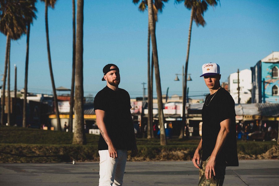 Portrait of music duo Lost Kings. They stand in the street in Los Angeles, palm trees behind them.