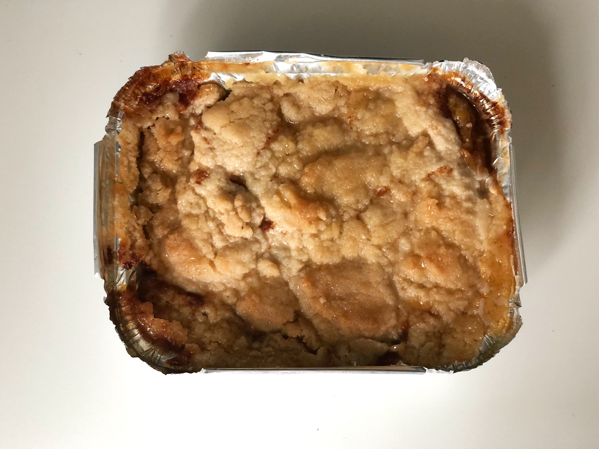 On a white table, a tin foil pan of peach cobbler is fresh from the oven and dark in the corners. Photo by Alyssa Buckley.