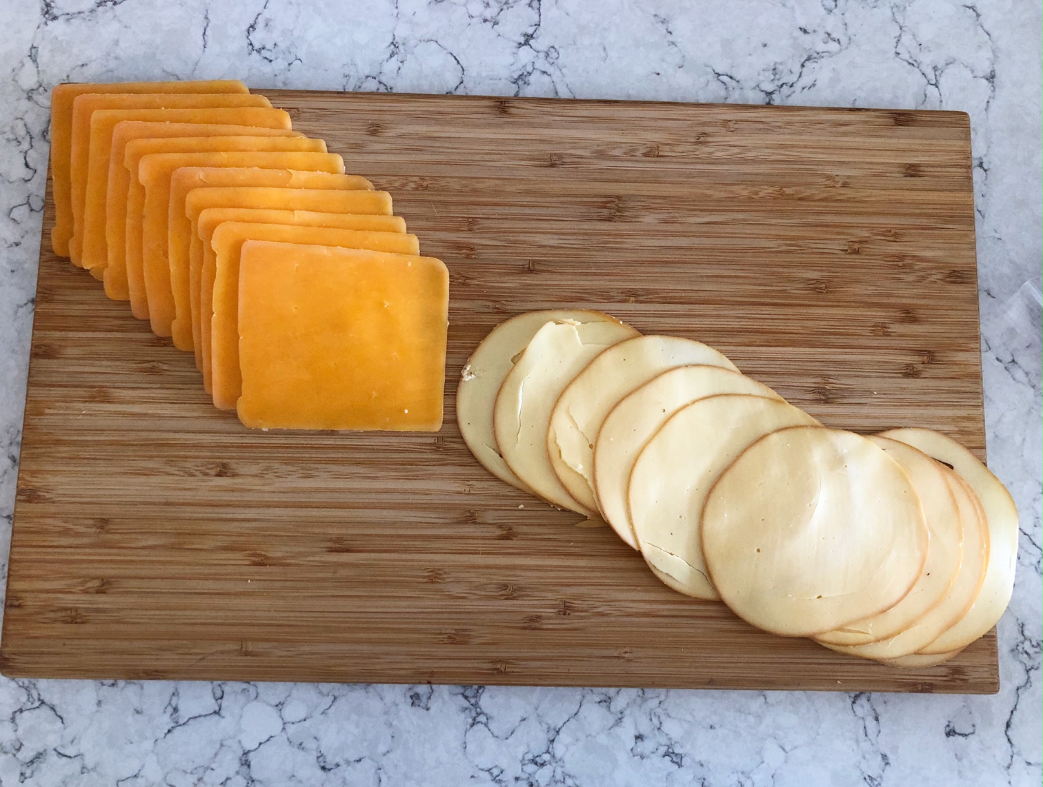 On a wooden cutting board, there are square slices of cheddar arranged in a diagonal meeting in the middle with circular slices of gouda cheese. Photo by Alyssa Buckley.