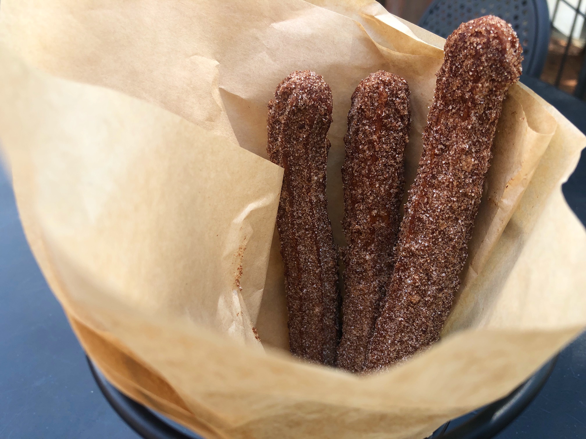 In brown parchment paper inside a black metal cone at Maize at the Station in Downtown Champaign, there are three long churros dusted with cinnamon sugar. Photo by Alyssa Buckley.