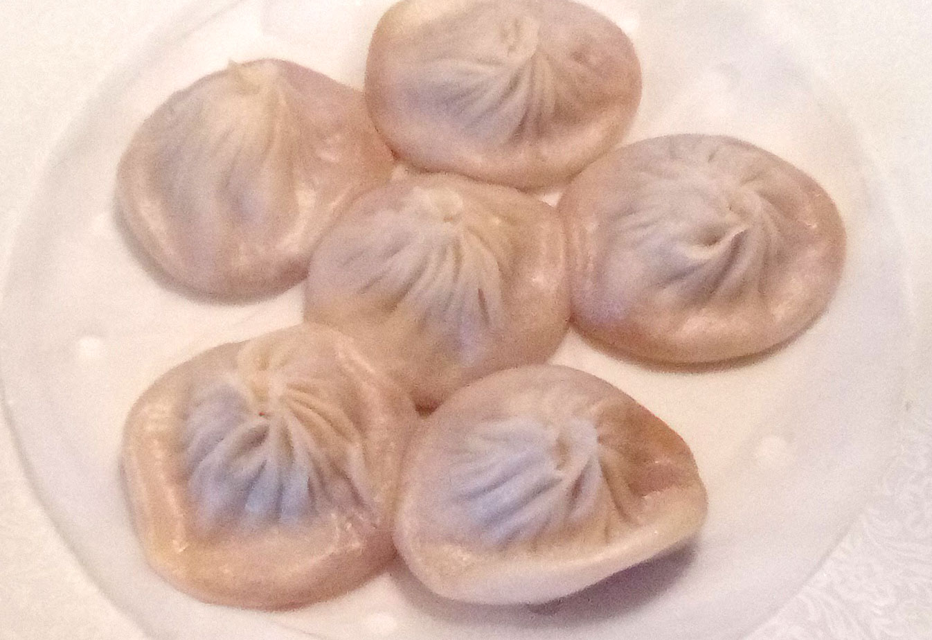 On a white plate, there are six steamed dumplings with rippled middles. Photo by Paul Young.