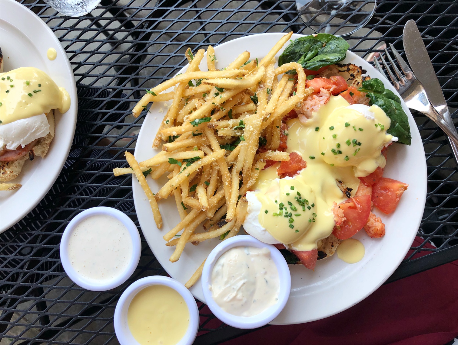 On a black patio table at Sunsinger, there is a white plate with fries and two eggs benedict. There are three small cups of sauces beside the plate. Photo by Alyssa Buckley.