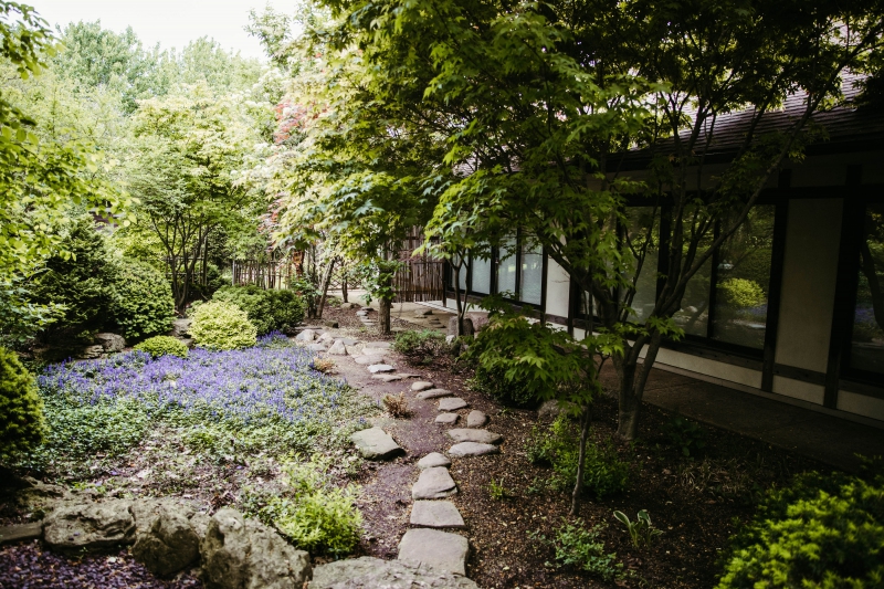Japan House garden with a stepping stone path. There are shrubs, trees, and flowers framing the path. Photo by Anna Longworth.