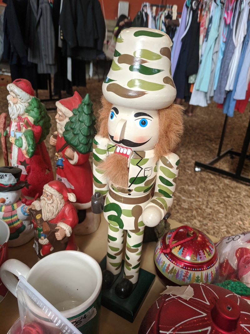 A nutcracker figure wearing camouflage. It is sitting on a table of other Christmas decorations. Photo by Tom Ackerman.