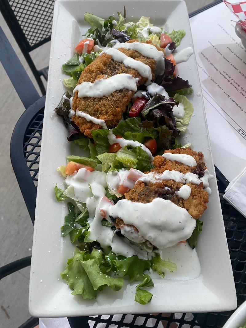 A white rectangular plate is topped with mixed greens salad with chopped red tomatoes, two large fried mushrooms, and a drizzle of ranch dressing. Photo by Julie McClure.
