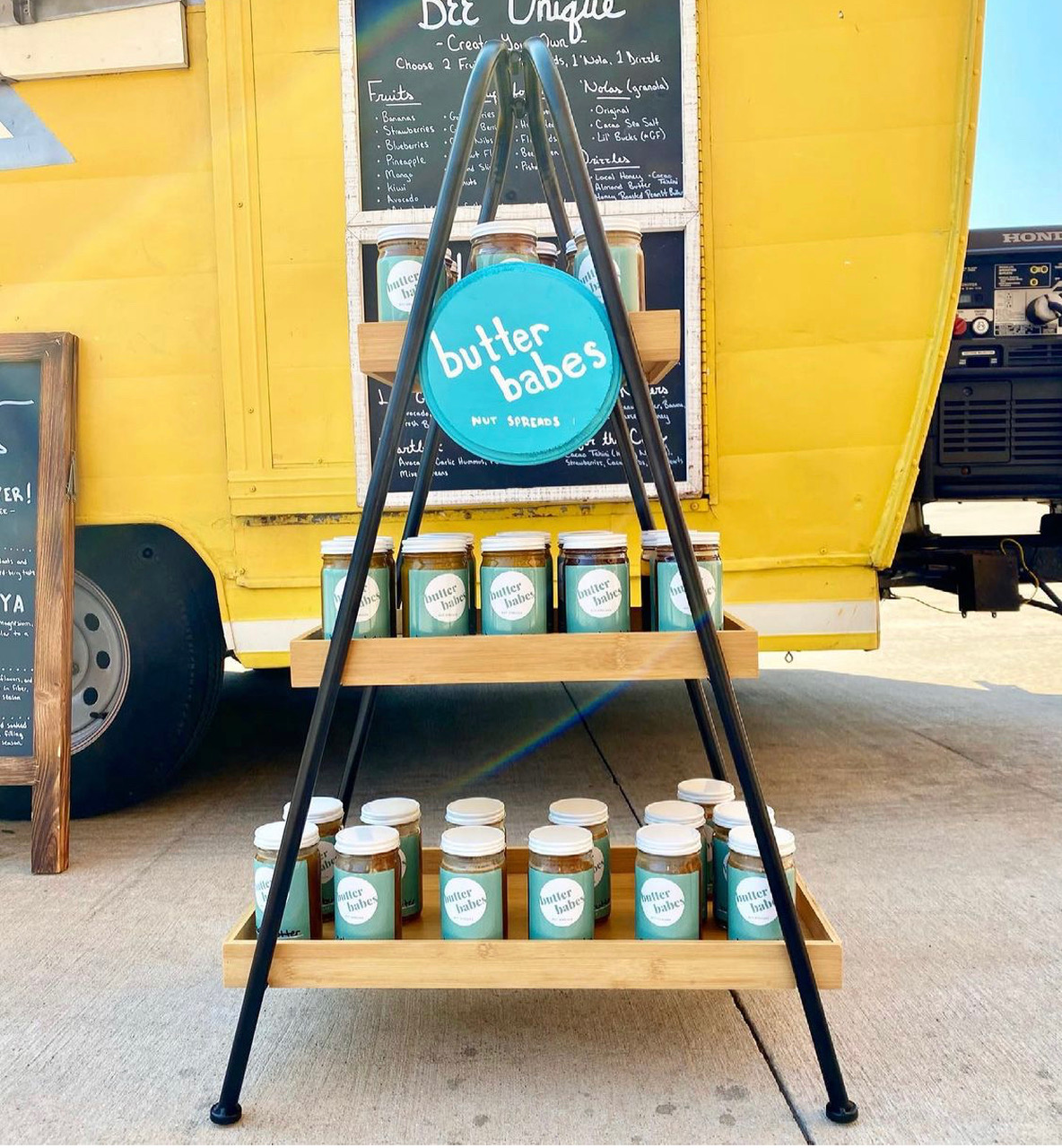 In front of the Just BEE Acai truck, there is a triangular stand holding the glass jars of nut butter from Butter Babes. Photo from Butter Babe's Instagram page.