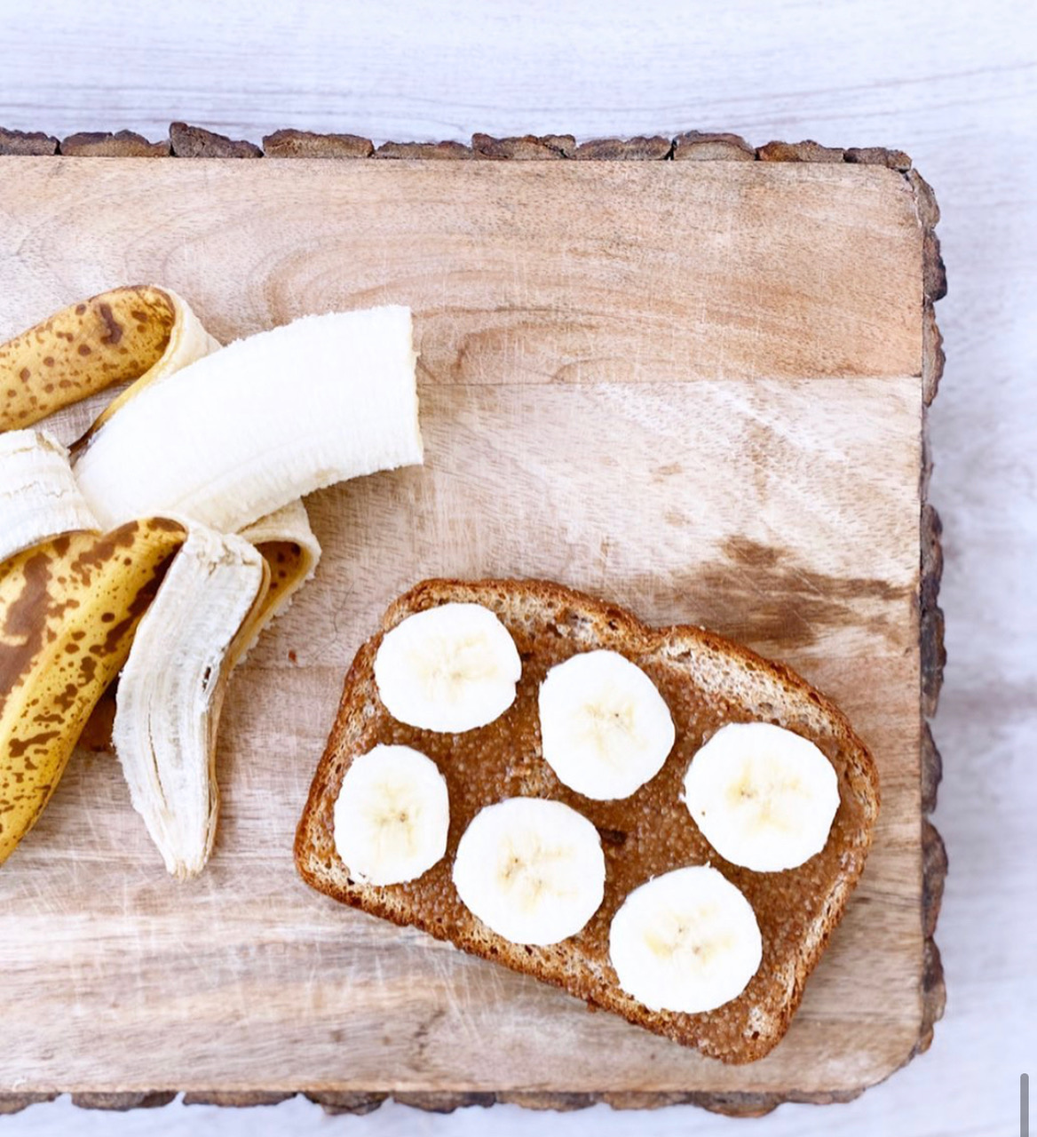 On a raw edge wooden cutting board, there is a slice of bread with nut butter and circles of sliced banana. Photo from Butter Babe's Instagram page.