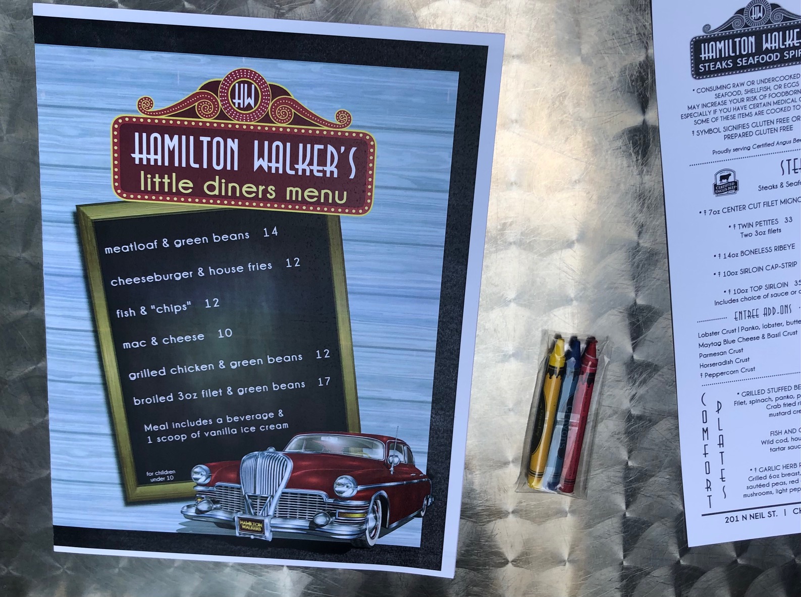 On a silver table at Hamilton Walker's in Champaign, Illinois, there is a kids' menu with a plastic wrapped set of crayons. Photo by Alyssa Buckley.