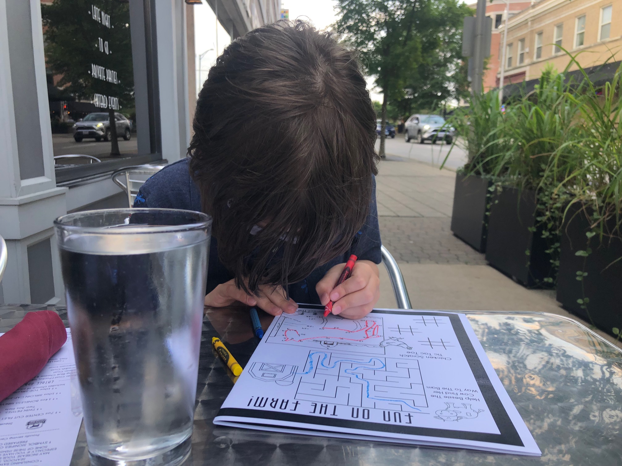 A white boy colors on his kids' menu on a silver table outside in Downtown Champaign. Photo by Alyssa Buckley.