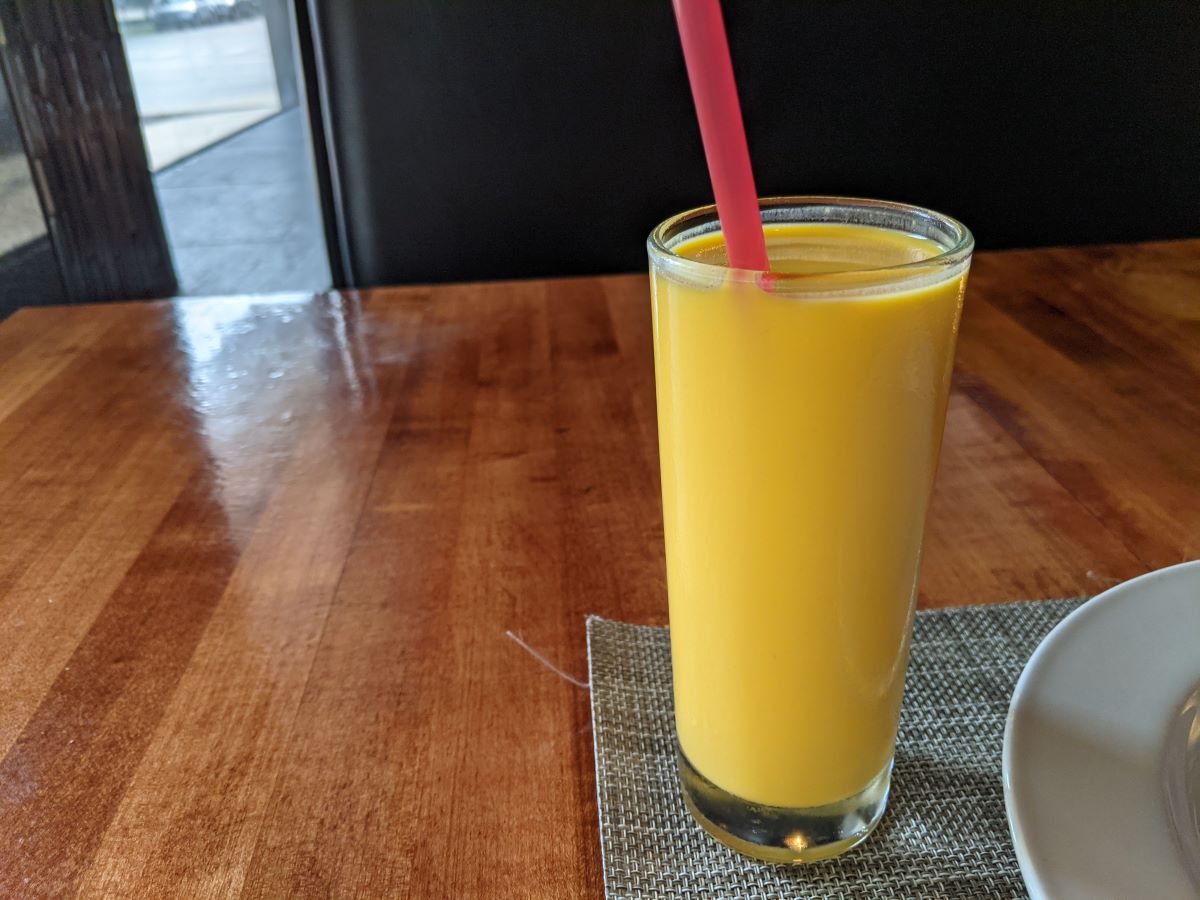 An orange beverage in a tall glass with a red straw. Photo by Tias Paul.