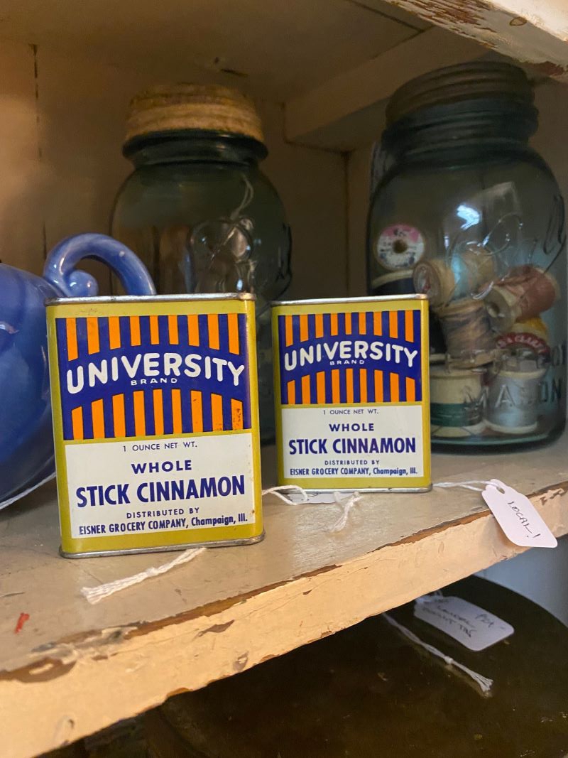 Two rectangular cinnamon containers are side by side on a shelf. There are orange and blue stripes on it and says University Brand. Photo by Julie McClure.