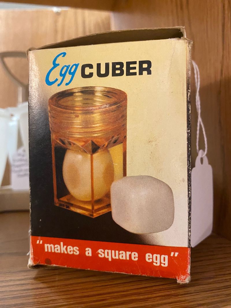 A small rectangular box has a photo of a cylinder with an egg in it, and a cube shaped egg next to it. The box says Egg Cuber. Photo by Julie McClure.