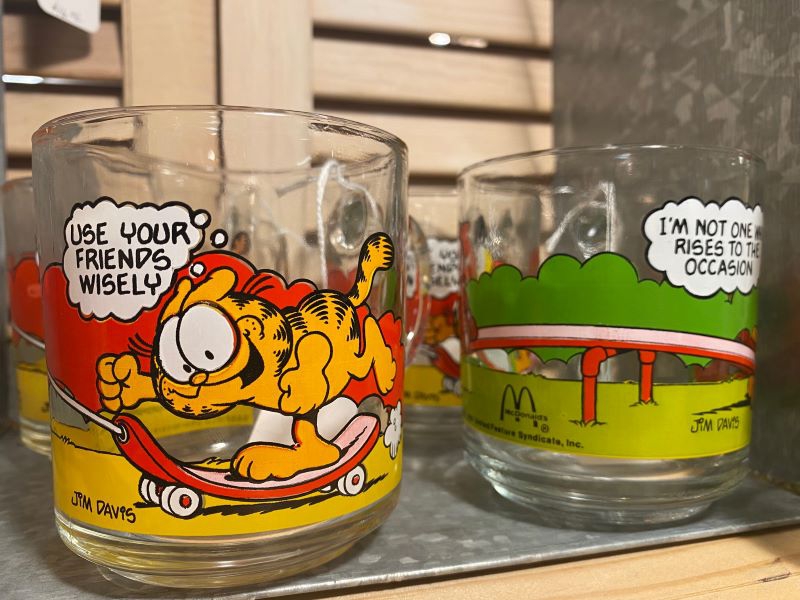 Two glass mugs with the orange Garfield cartoons on them sit side by side on a shelf. Photo by Julie McClure.