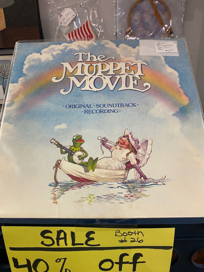 An album cover with blue sky, clouds, and a rainbow. Kermit the Frog and Ms. Piggy are sitting in a boat on the water. It says The Muppet Movie at the top. Photo by Julie McClure.