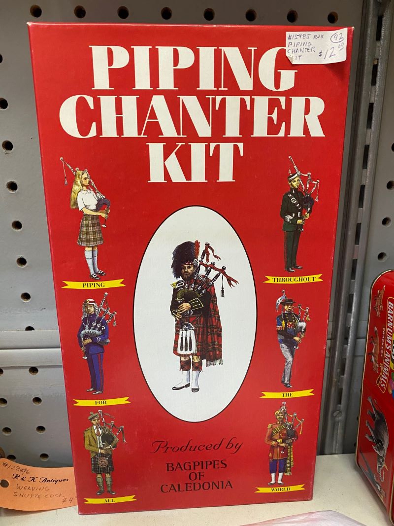 A rectangular red box has drawings of bag pipers on it. It says Piper Chanting Kit in white block letters. Photo by Julie McClure.