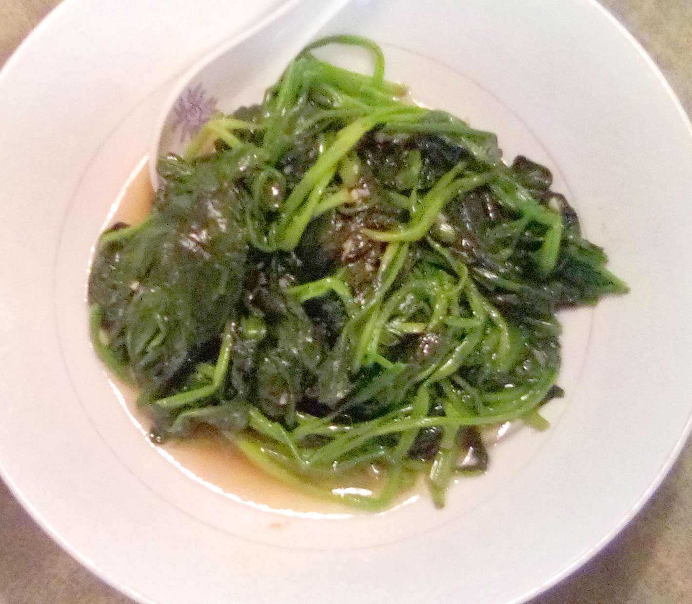 On a white plate, there is a circular serving of spinach, wilted and in a light sauce. Photo by Paul Young.