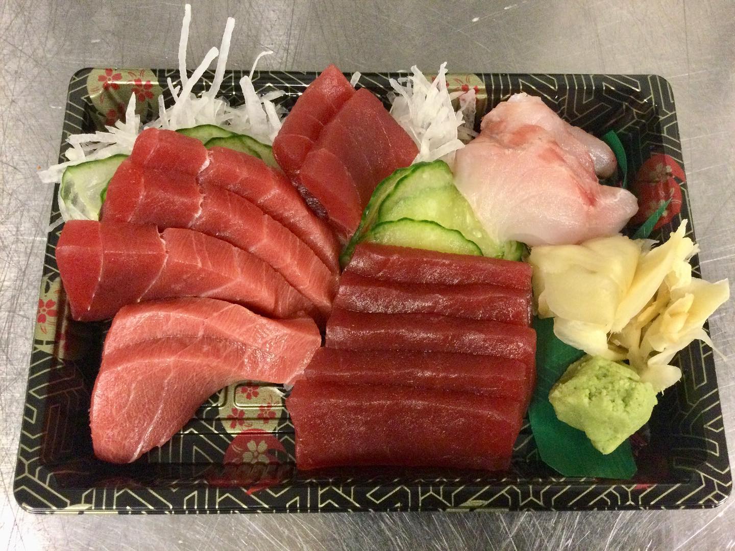 Many slices of sashmi are arranged in a paper rectangular container with thinly sliced cucumbers in the middle. Photo by Ken Ishibashi.