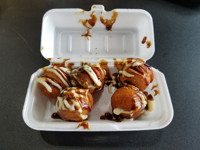 Five Takoyaki covered in sauce held in a Styrofoam container. Photo by Matthew Macomber.