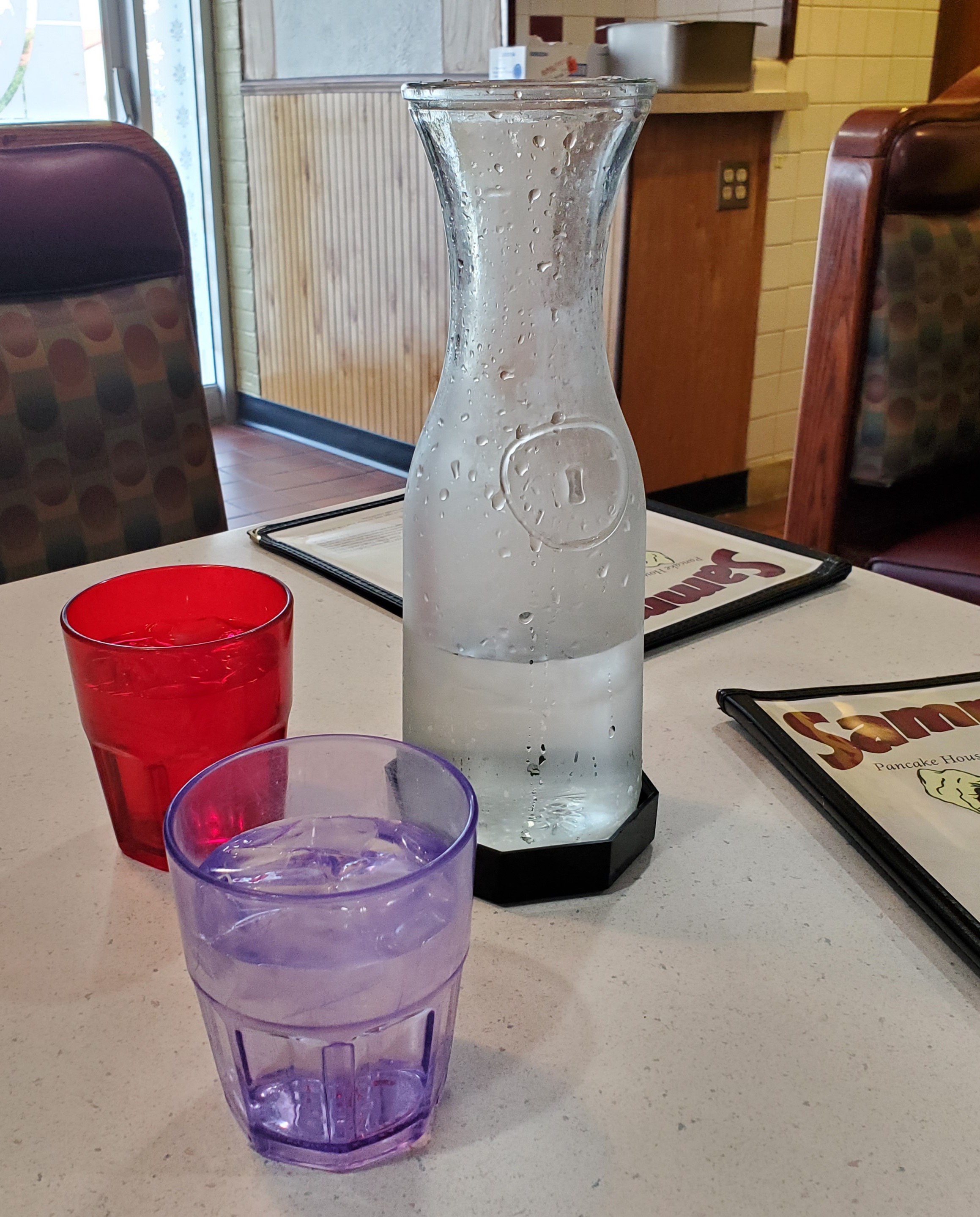 On a white speckled diner table, there are two small glasses of water and a large carafe of water. Photo by Carl Busch.