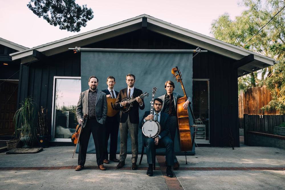 The Punch Brothers stand in front of a photography studio backdrop, holding their instruments. 