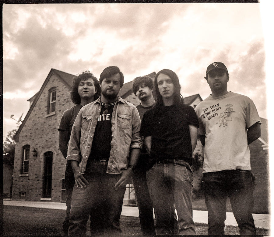 Sepia toned image of the band Rookie, standing in front of a brick house.