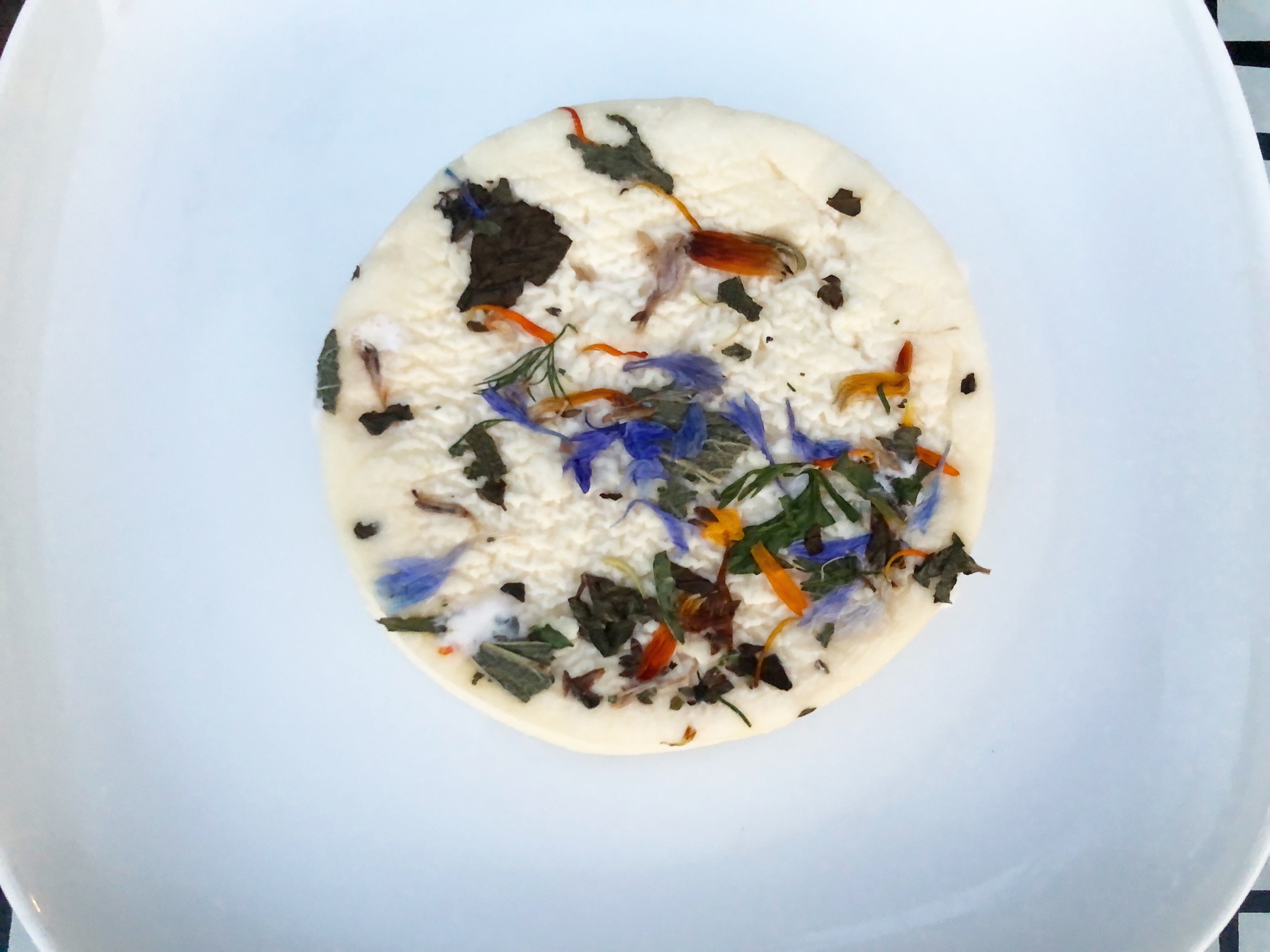 On a white plate, a bloomy rinded cheese is adorned with edible flowers. Photo by Alyssa Buckley.
