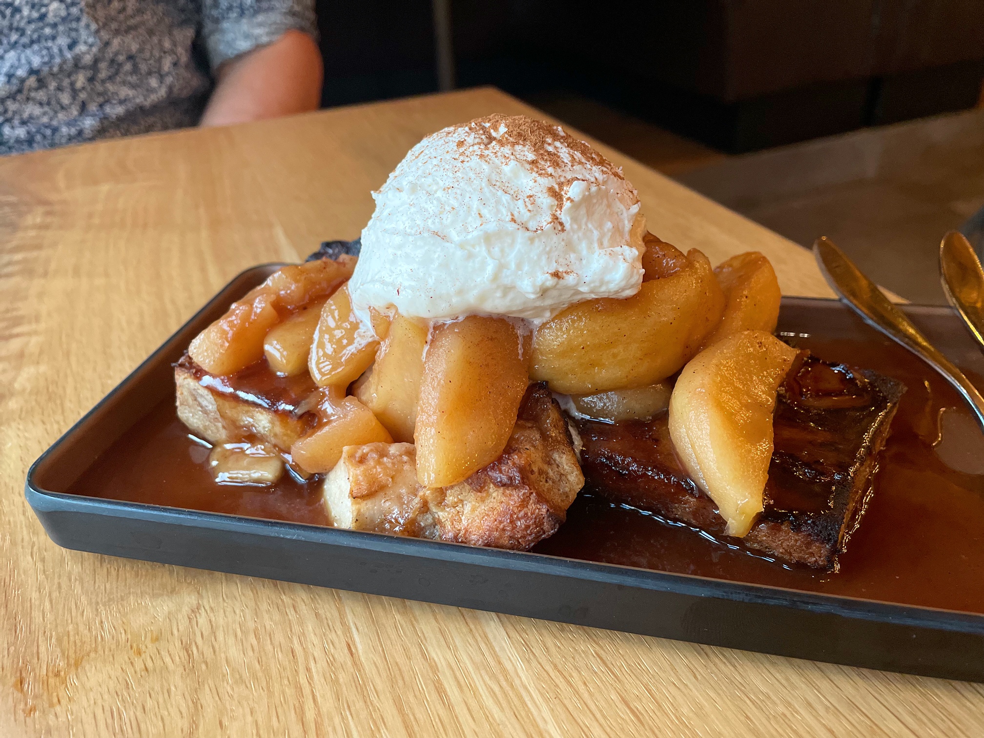 On a wooden table, there is a dessert with apples, bread, and a big scoop of a cream topping. Photo by Alyssa Buckley.