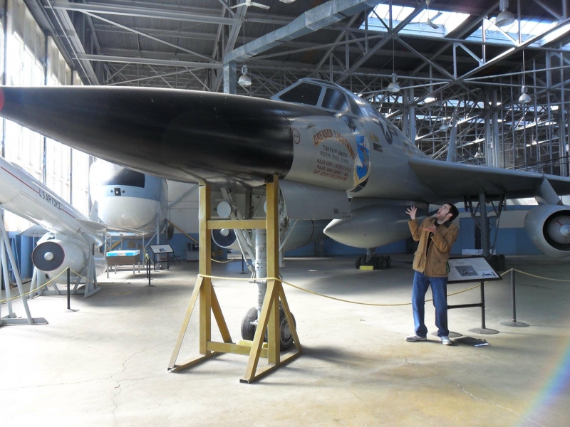 The writer is standing underneath a plane in a hanger. He is holding his hands up and looking surprised. Photo by Marlene Brawner.