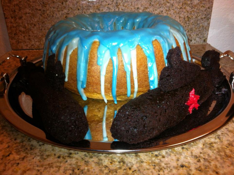 A bundt cake with blue and white icing dripping down the sides. It's flanked by two submarines made out of chocolate cake and sitting on a platter. Photo by Charles Bjork.