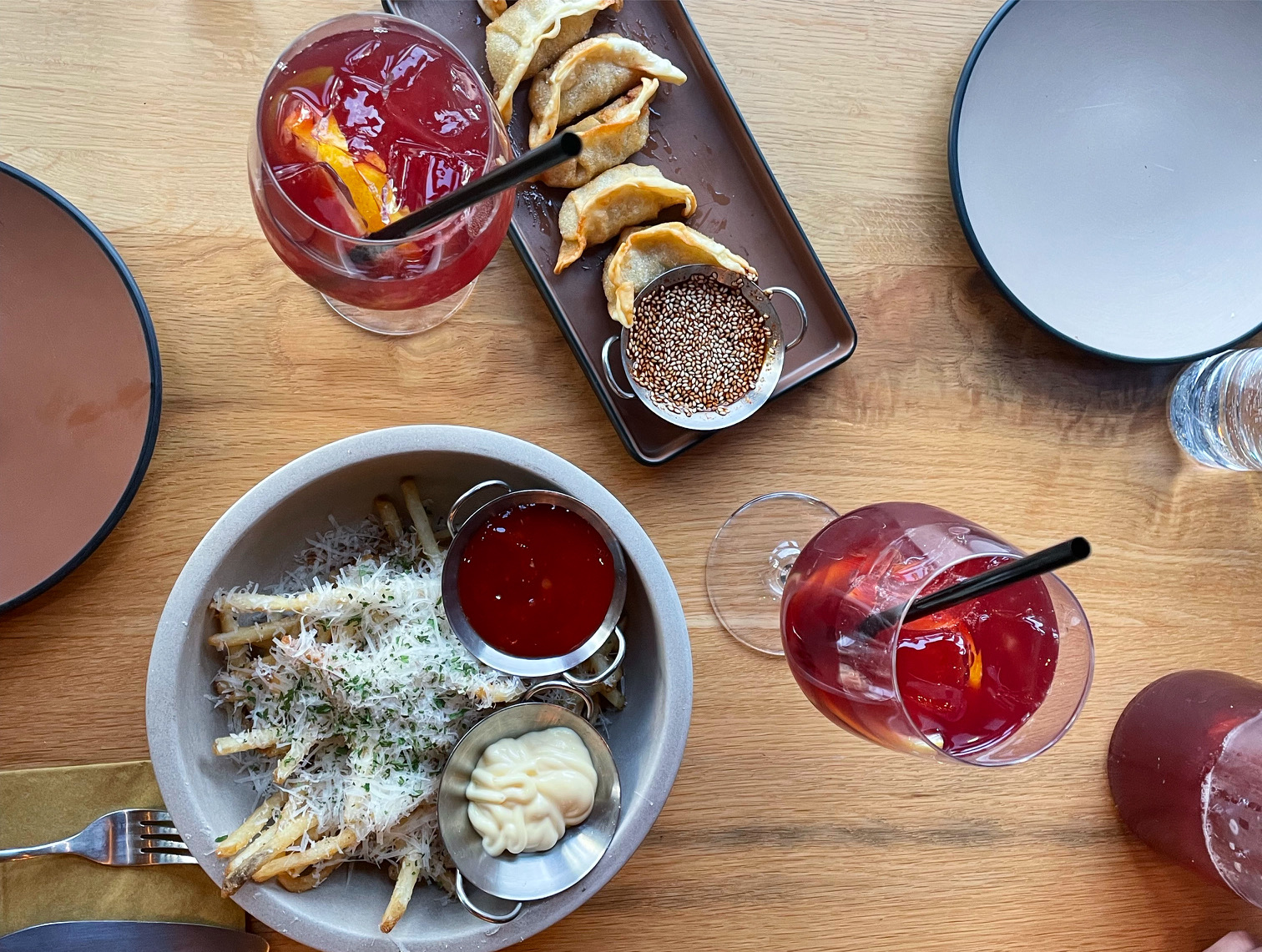An overhead photo shows a light wooden table with two wine glasses filled with sangria, a rectangular plate of fried dumplings with a little dipping sauce full of sesame seeds, and a bowl of fries covered in Parmesan cheese. Photo by Alyssa Buckley.