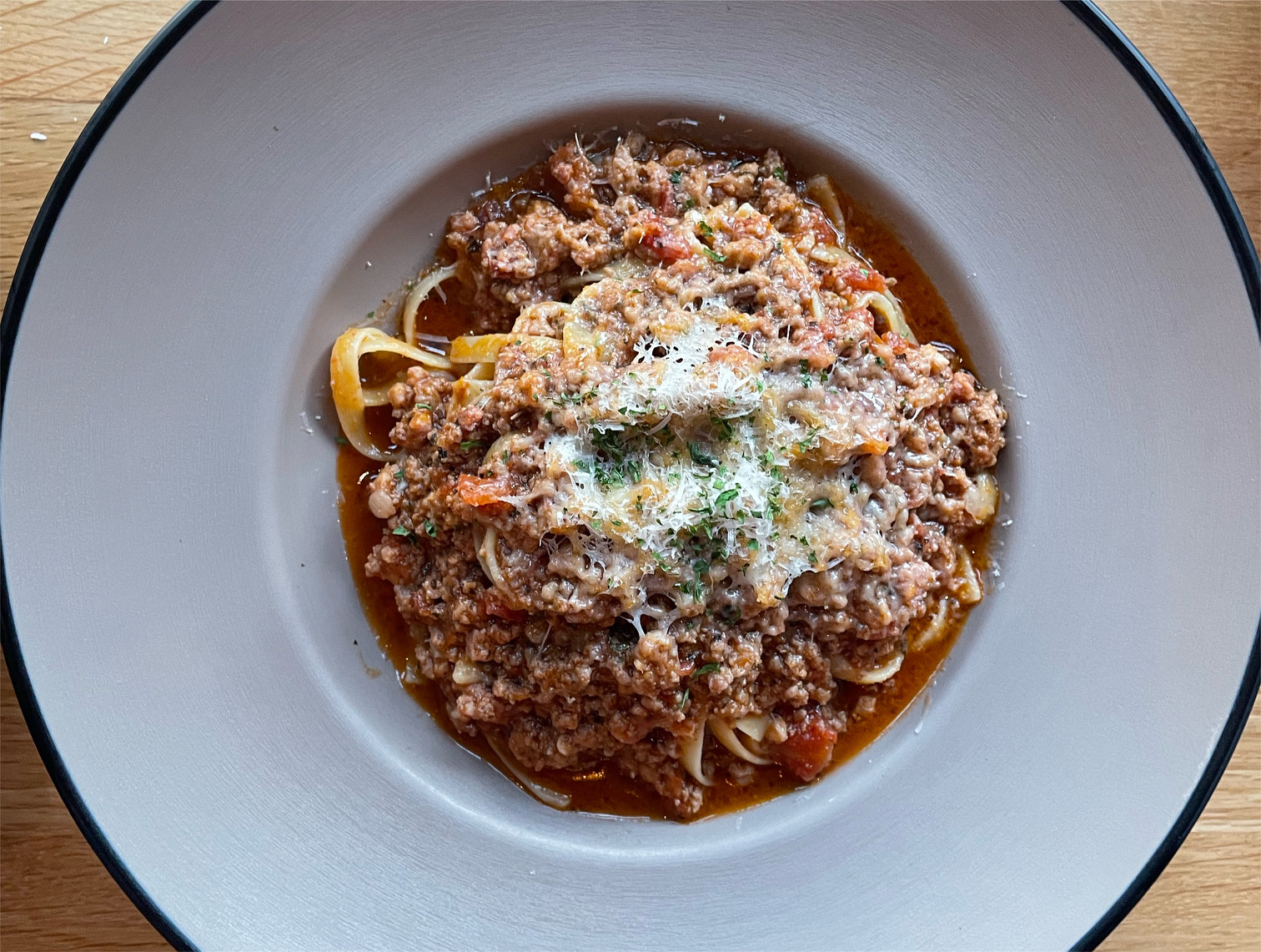 An overhead photo shows a gray bowl with the center full of a bolognese pasta with a big outer rim on the plate. Photo by Alyssa Buckley.