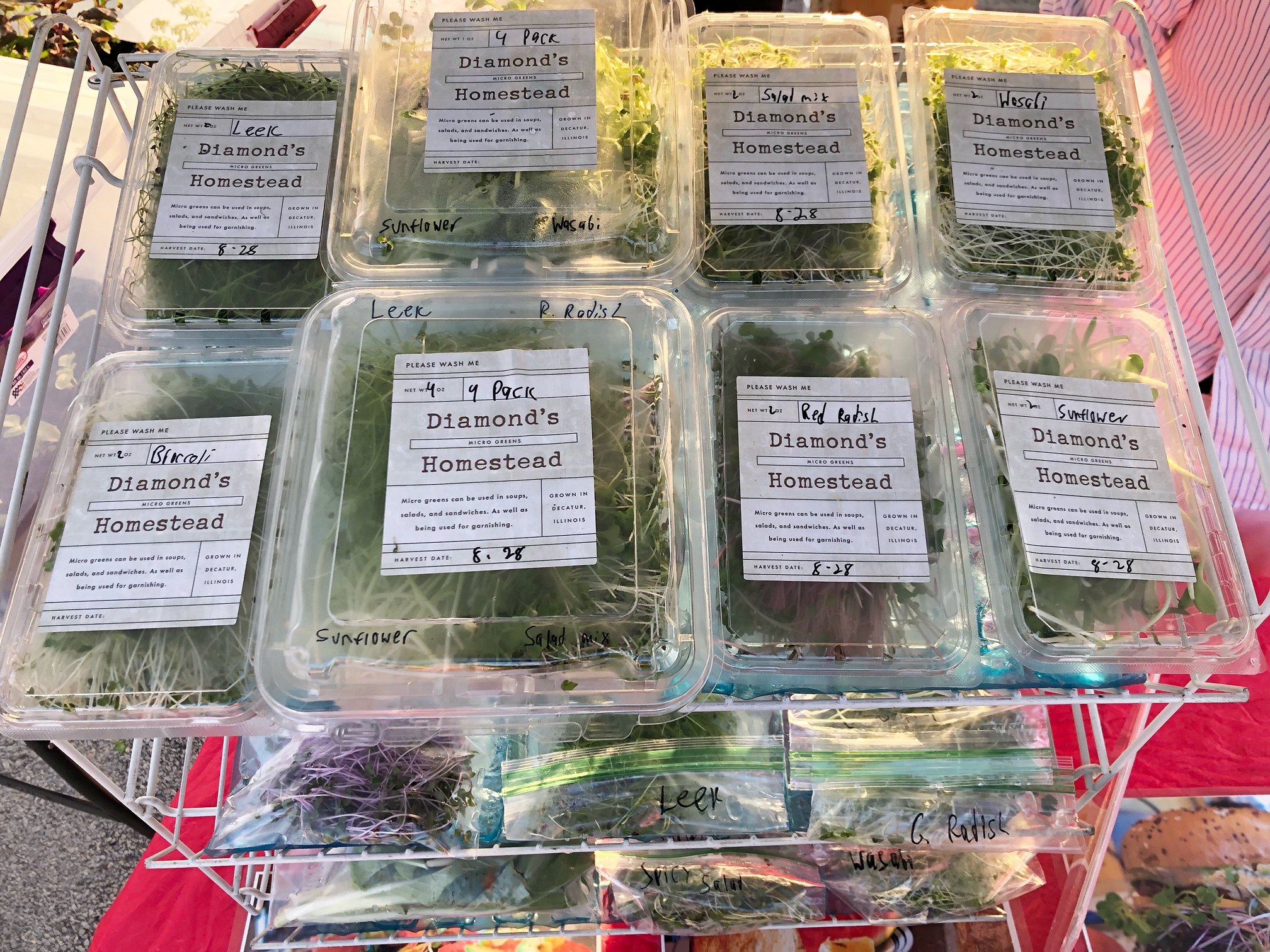 On a tiered, white plastic stand, there are many plastic clamshell containers filled with microgreens from Diamond's Homestead. Photo by Alyssa Buckley.